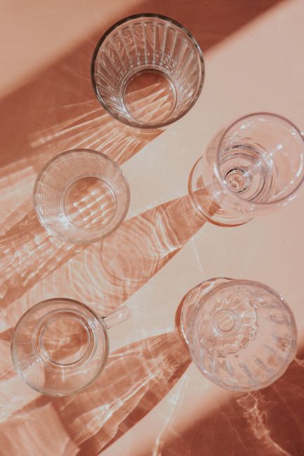 Top view of artistic glass cup shadows on a beige surface, creating abstract patterns.