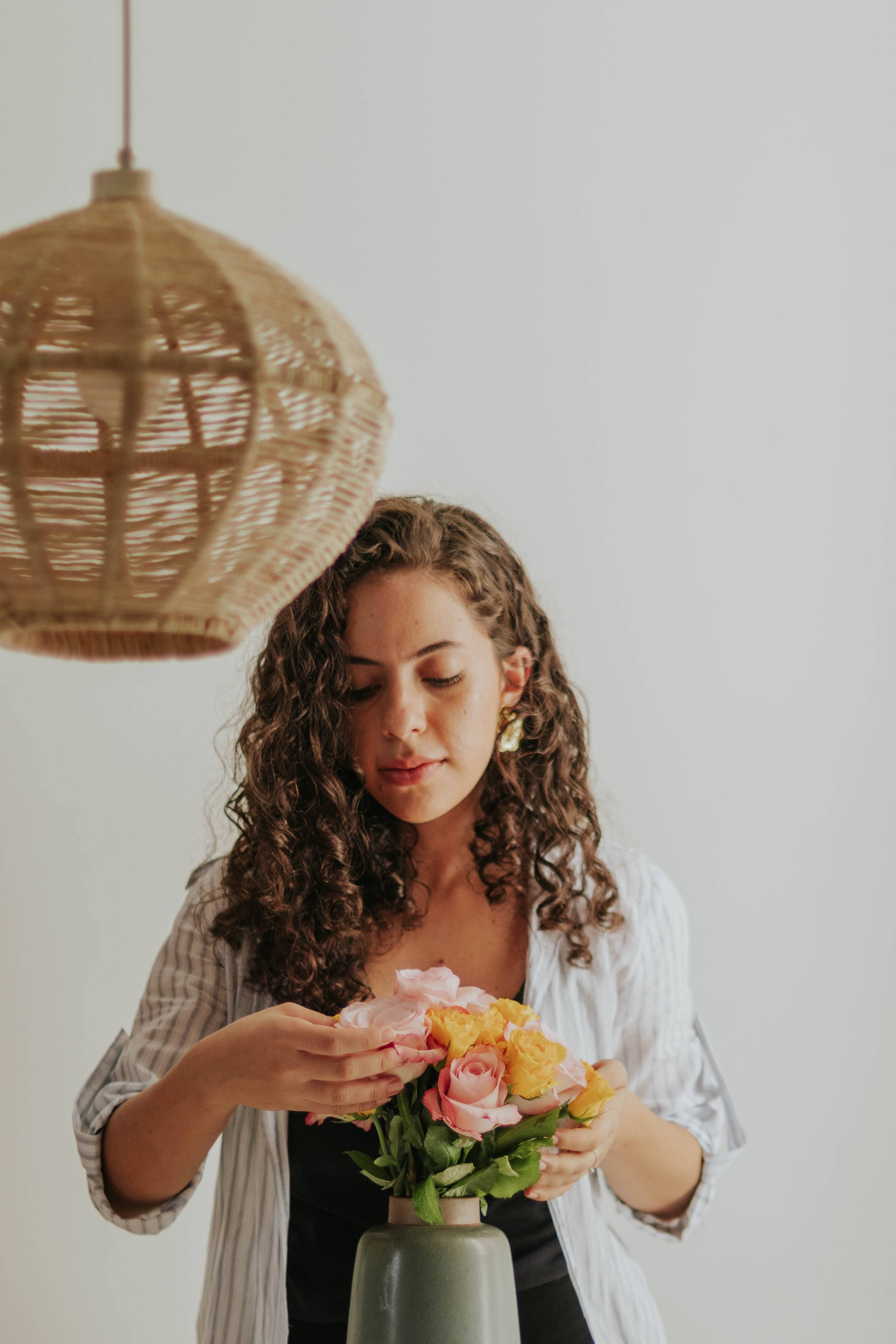 A woman arranging a bouquet of flowers indoors beneath a wicker pendant light.