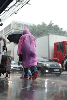 Urban landscape of people in rain with umbrellas and raincoats on busy street.