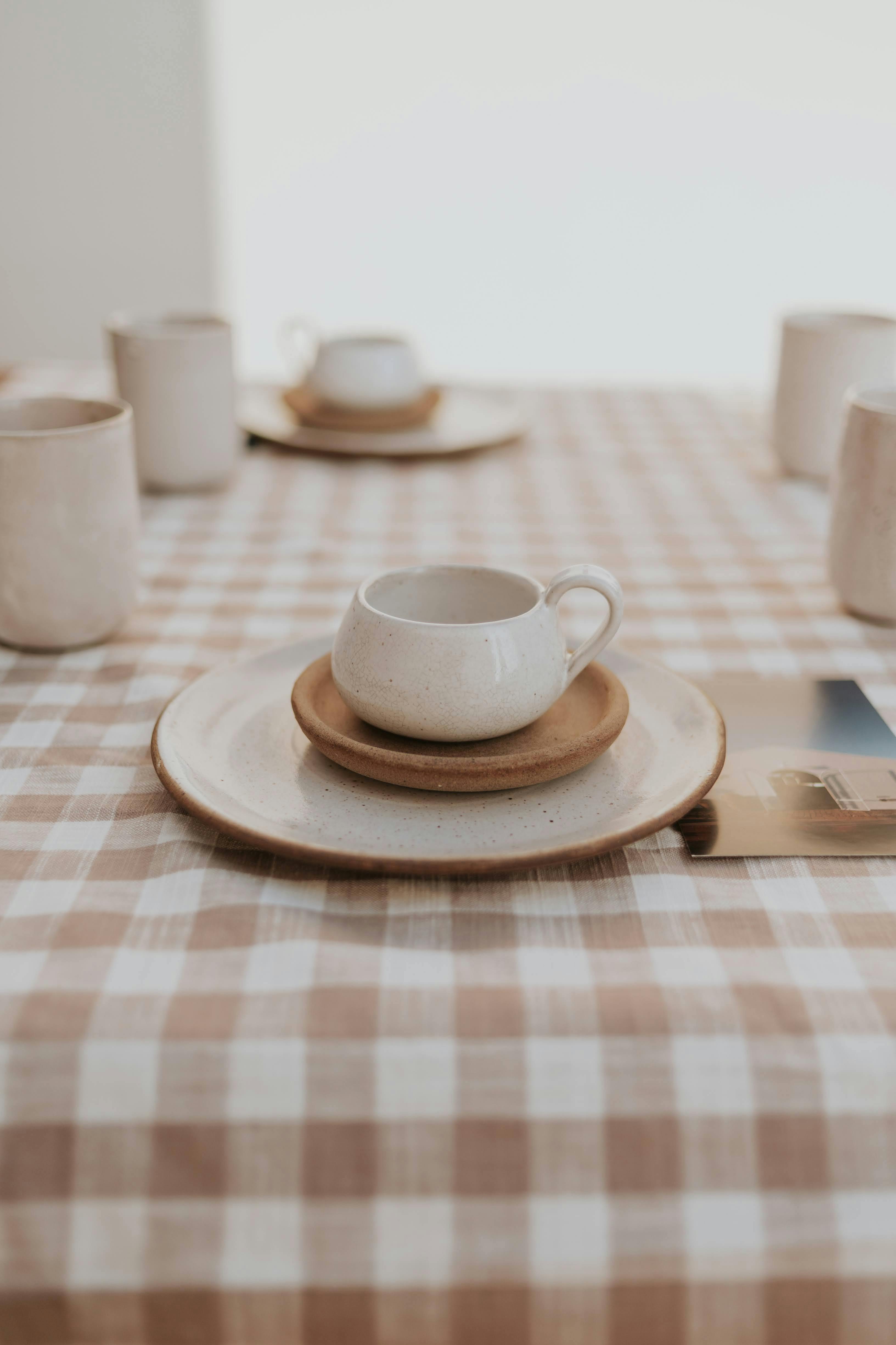 Elegant display of ceramic tableware on a checked tablecloth in soft natural lighting.