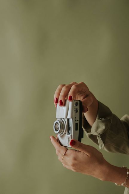 Aesthetic close-up of female hands with red nails holding a vintage camera against a muted background.