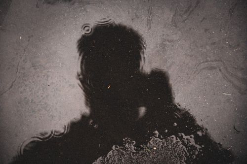 Free Dark silhouette of a person reflected in a rain-covered puddle, creating a mysterious and artistic effect. Stock Photo