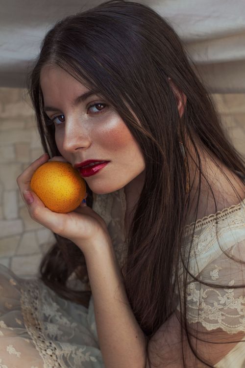 Free Stylish portrait of a woman holding an orange, showcasing elegance and natural beauty. Stock Photo