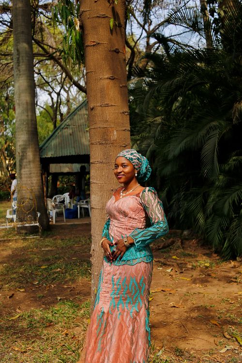 Free A woman in vibrant traditional Nigerian attire poses against a tree outdoors, capturing cultural elegance. Stock Photo