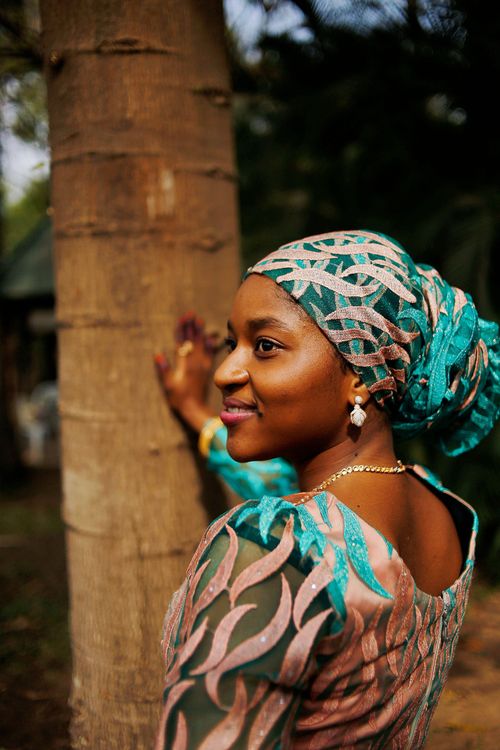 Free Portrait of a smiling woman in colorful attire leaning against a tree outdoors in Abuja, Nigeria. Stock Photo