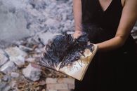 一名妇女拿着一本燃烧的书，室外烟雾和灰烬升腾