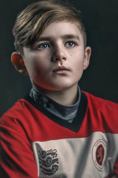 Captivating portrait of a young boy in a red sports jersey with striking blue eyes.