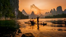 日落时分，渔民在一条宁静的河流上撒网，悬崖风景如画