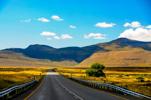 Free A scenic highway stretches through mountains and open fields under a bright blue sky. Stock Photo