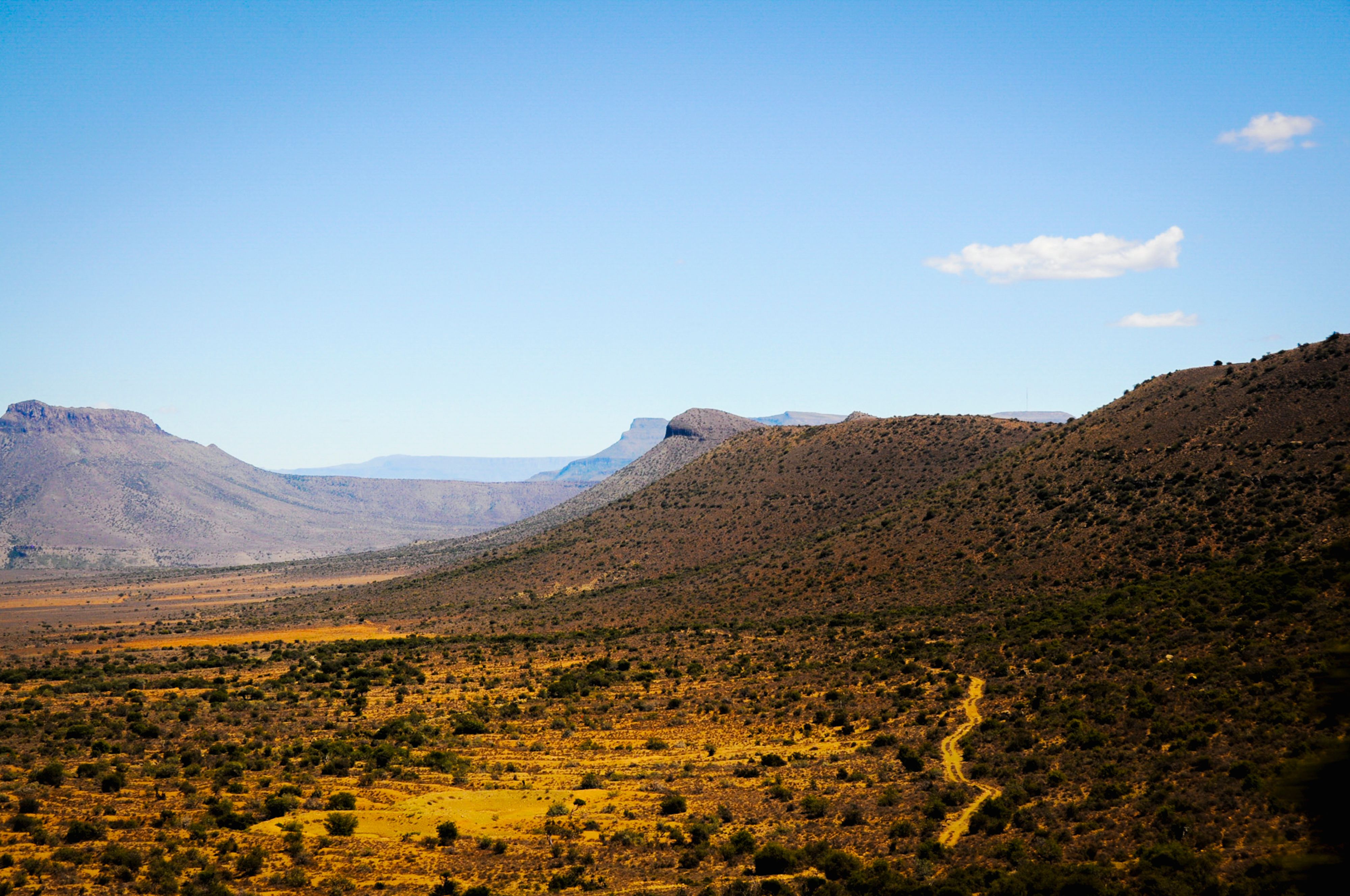 Scenic view of a vast, dry mountainous landscape under a clear blue sky.
