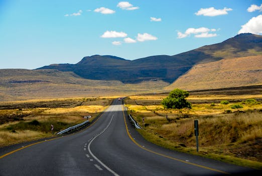 Wide open road leading into mountainous landscape under clear blue skies, ideal for travel inspiration.