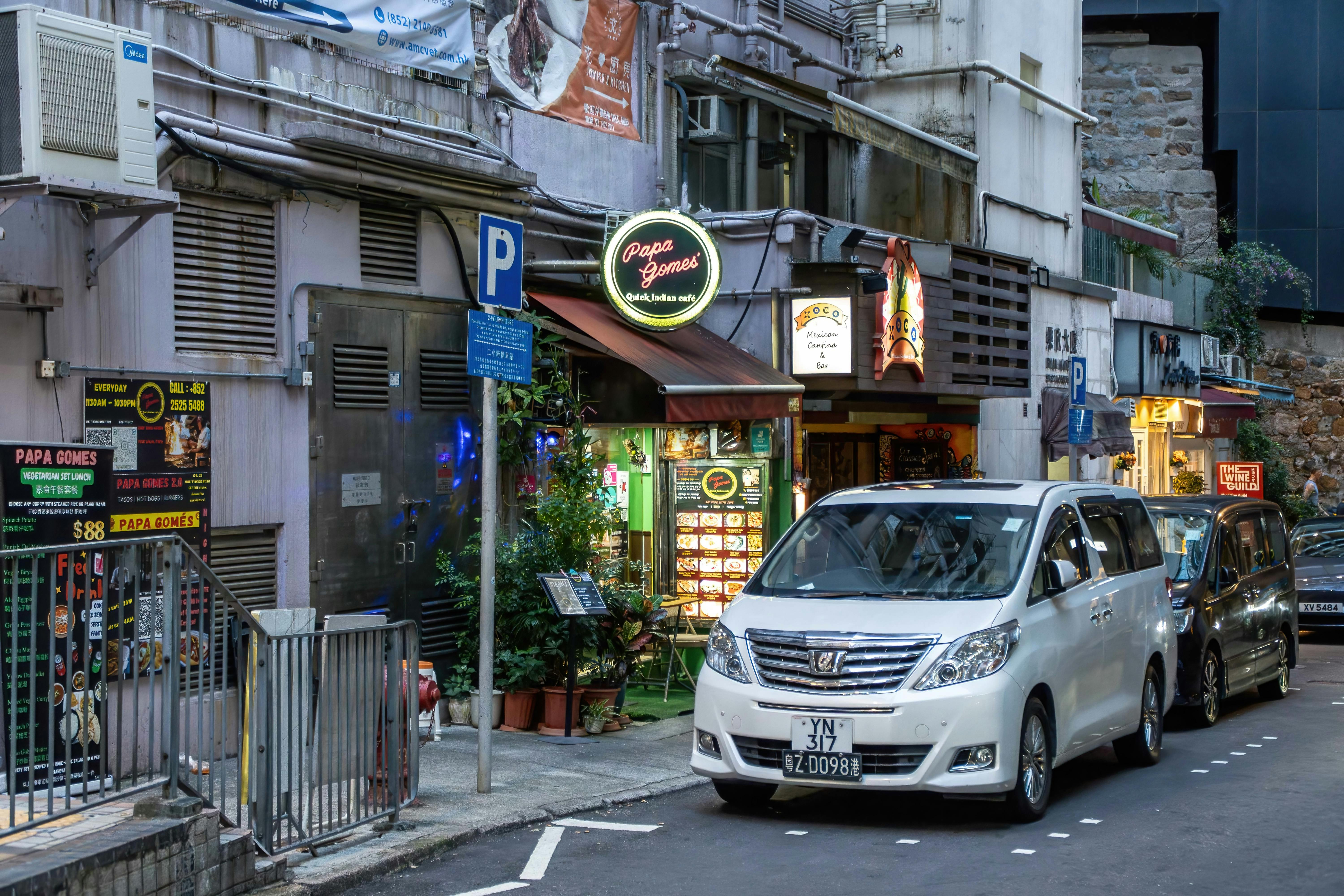 Charming street scene in Hong Kong featuring Papa Gomez restaurant and parked cars.