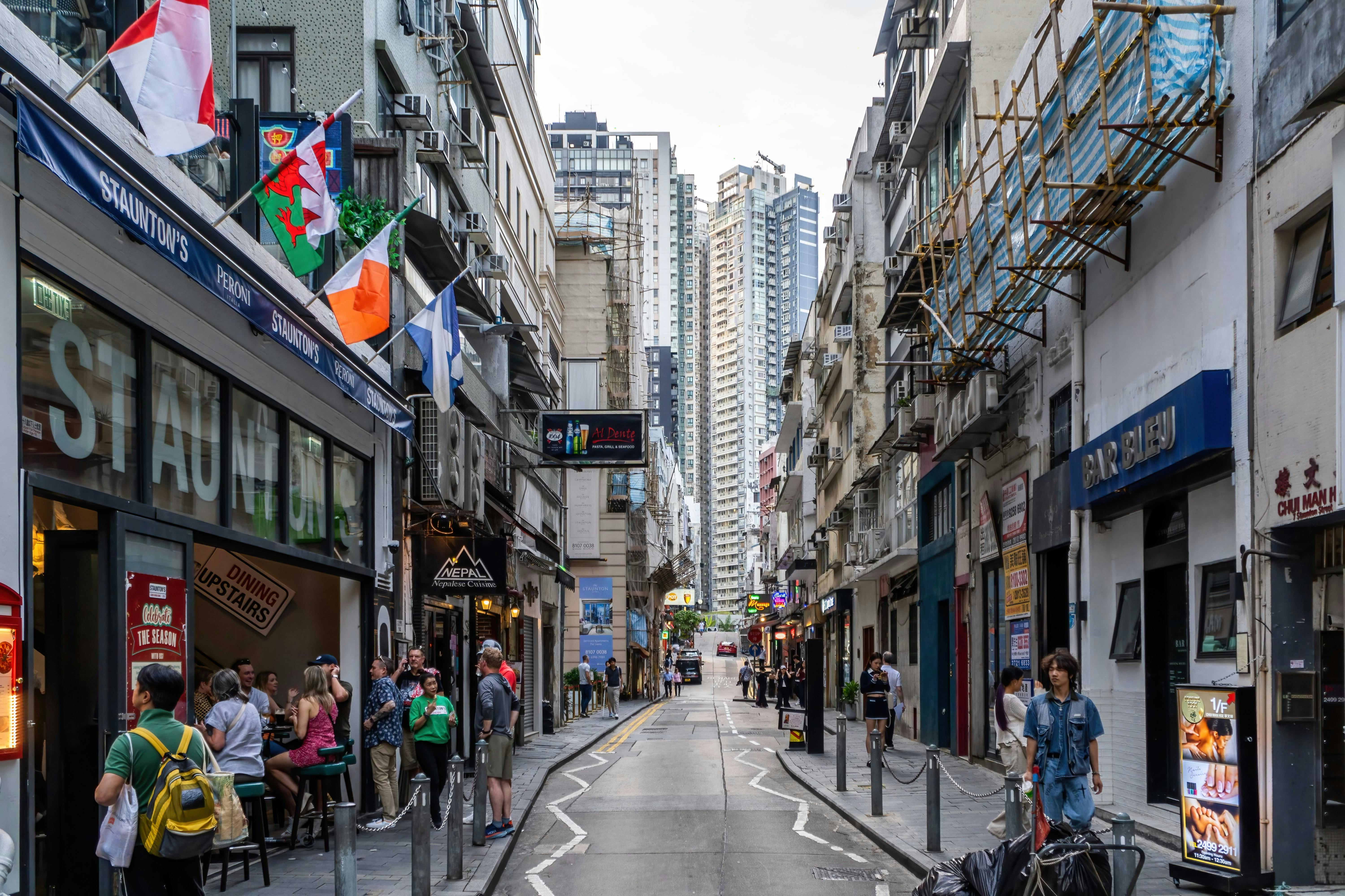 Lively street in Hong Kong's Soho district with people, restaurants, and skyscrapers.