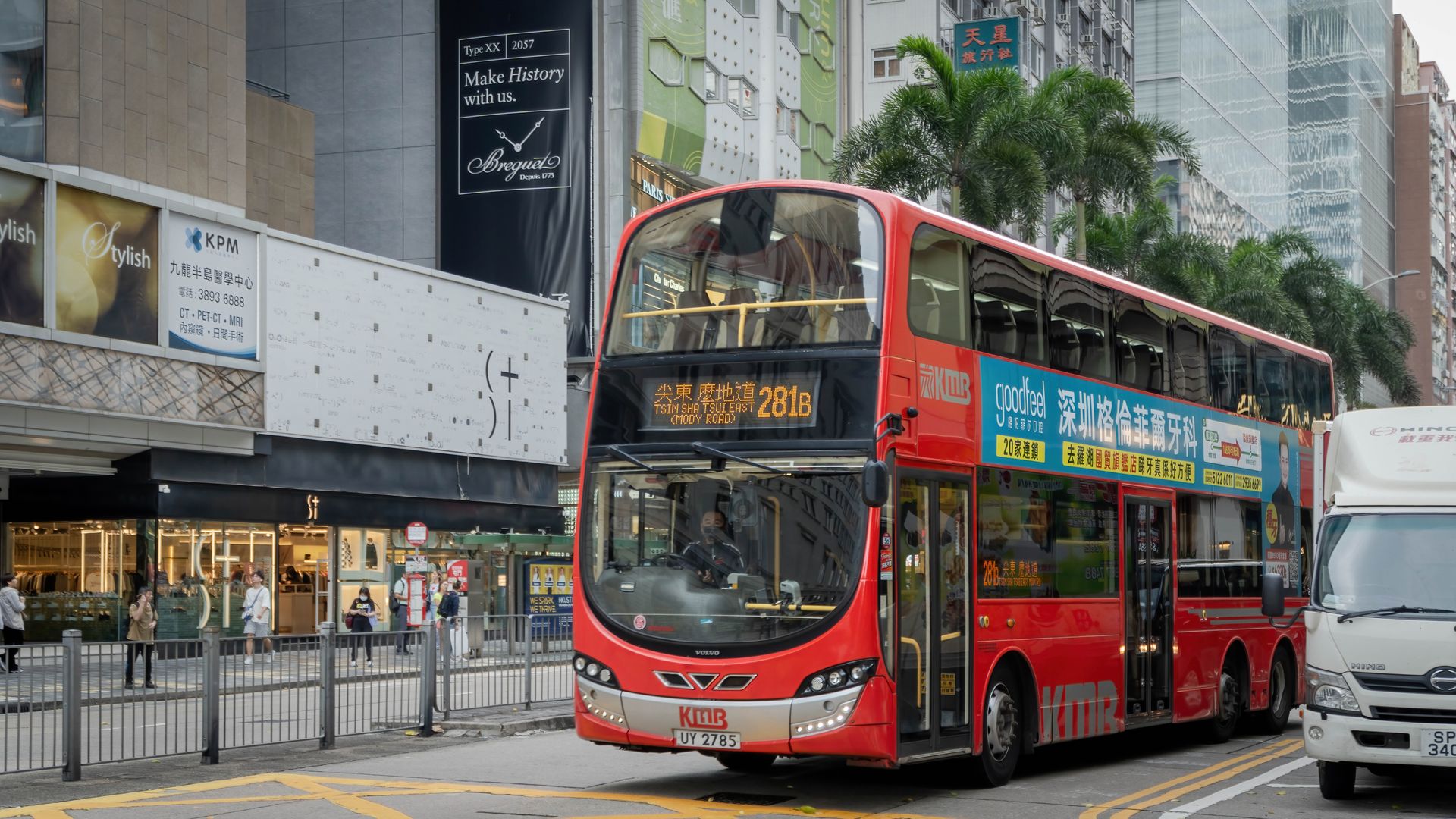 A vibrant red double-decker bus travels through a bustling Hong Kong street.