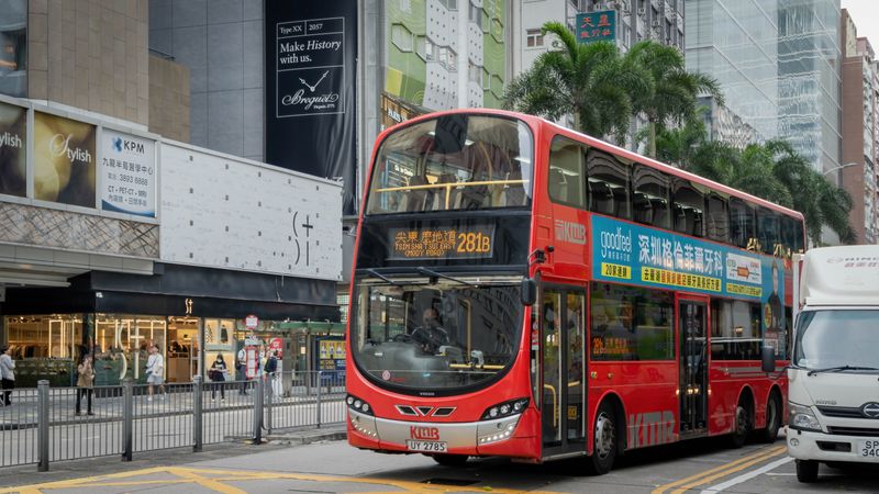 A vibrant red double-decker bus travels through a bustling Hong Kong street.