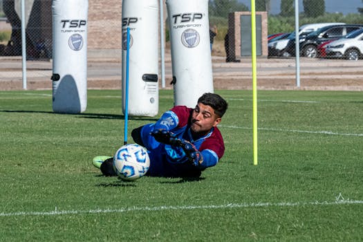Goalkeeper in action diving to save a soccer ball during practice on a sunny day.