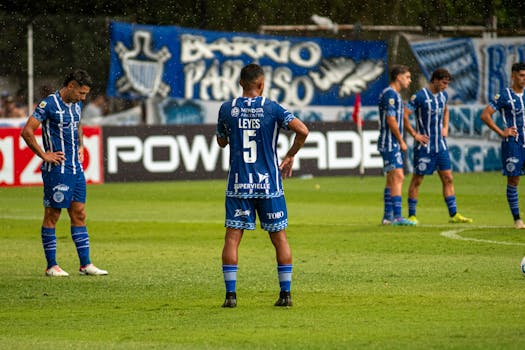 Soccer team in blue uniforms huddles on a rainy field, preparing for a match.