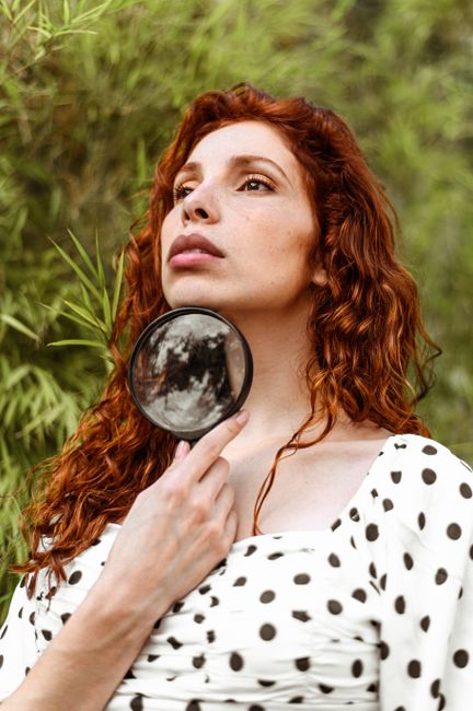 Portrait of a stylish woman outdoors holding a magnifying glass, showing elegance and fashion.