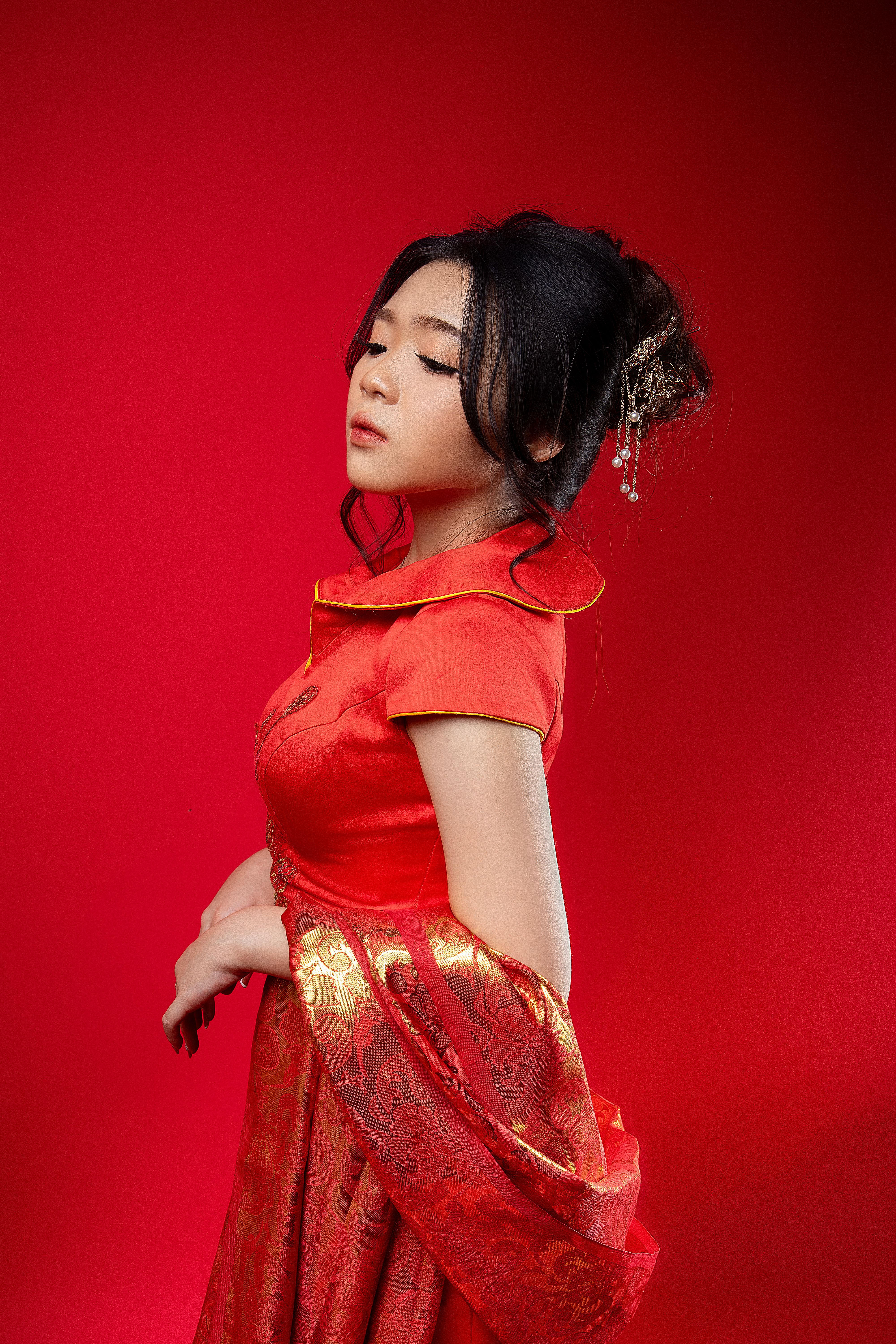Portrait of an Asian woman in a red dress with intricate designs, set against a vibrant red backgrou