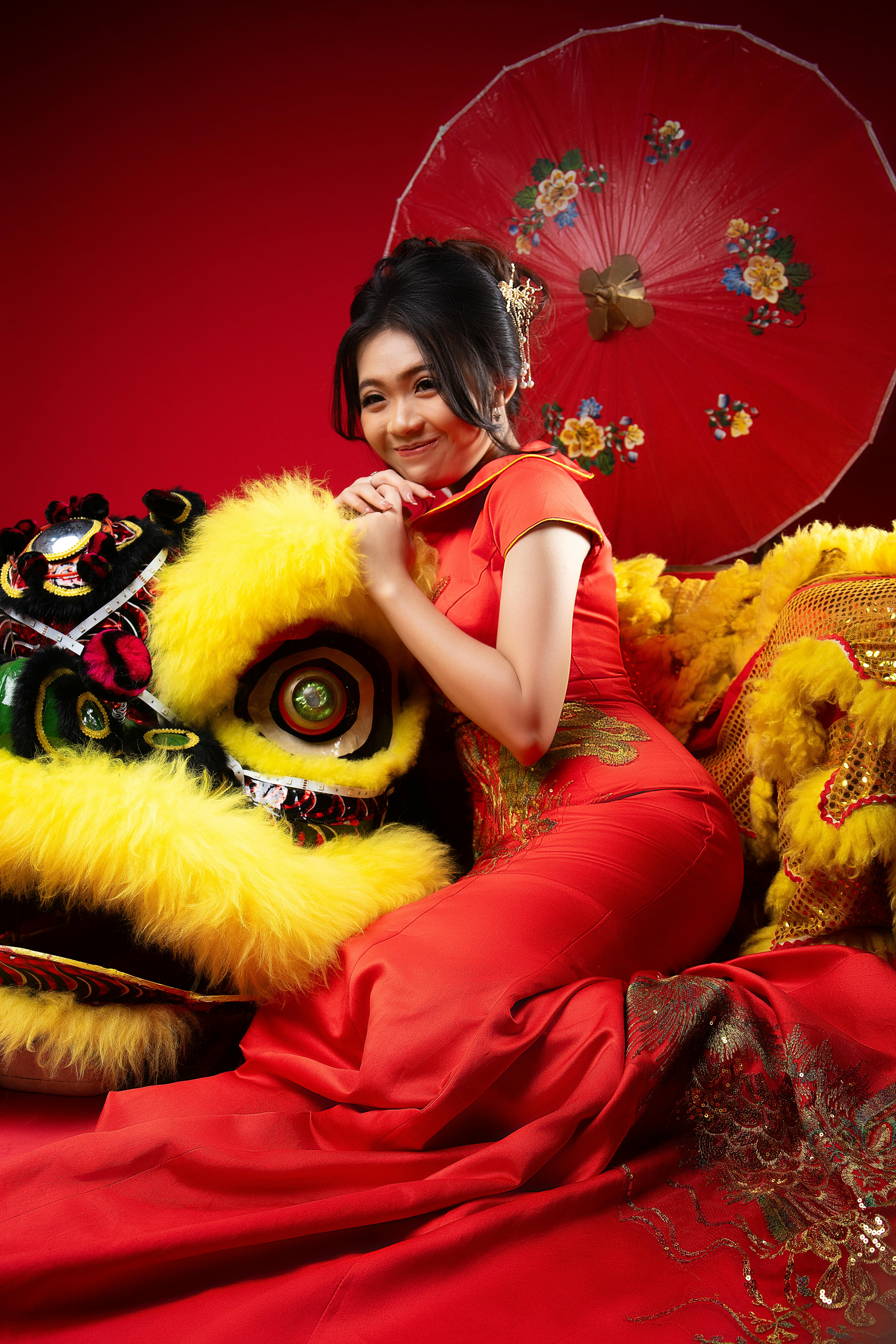 Woman in red cheongsam with lion dance costume in studio setting.