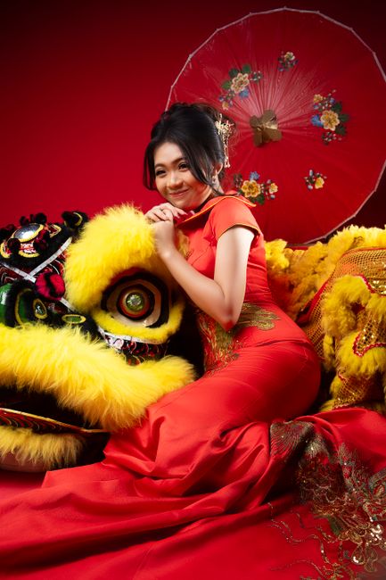 Woman in red cheongsam with lion dance costume in studio setting.