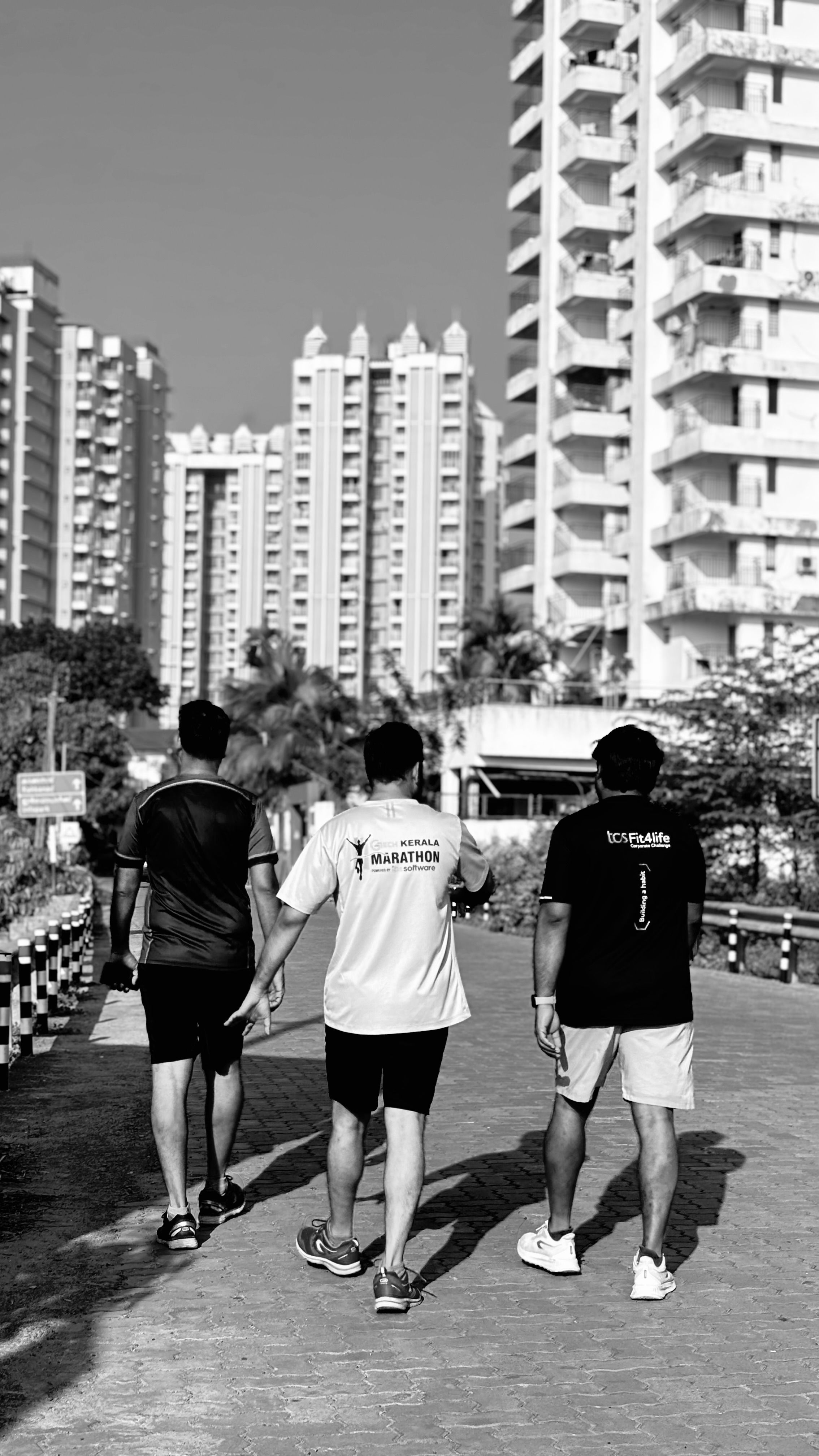 Three men walking on a pathway surrounded by tall buildings in Kochi, India.