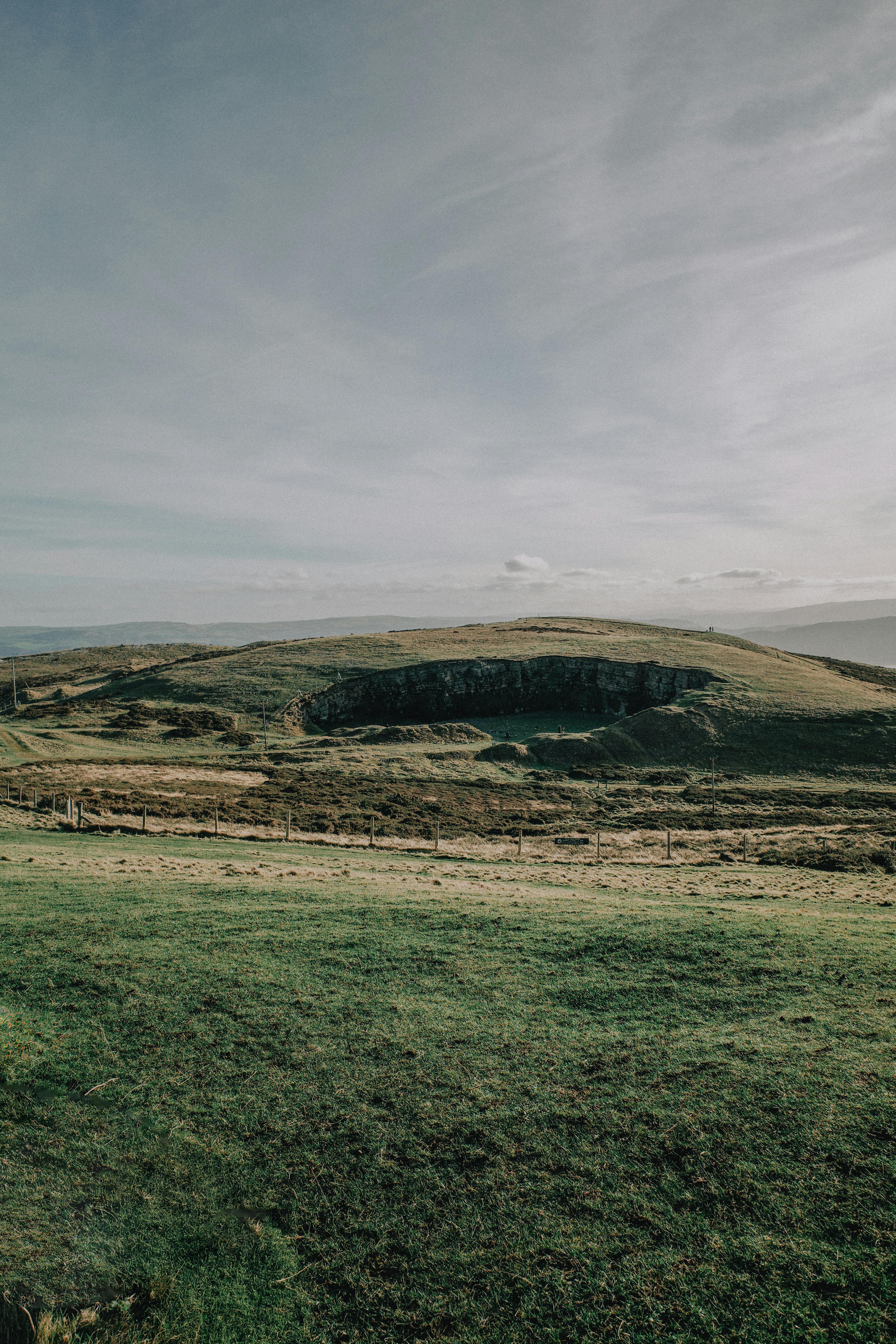 Expansive countryside landscape with grassy fields and distant hills on a cloudy day.