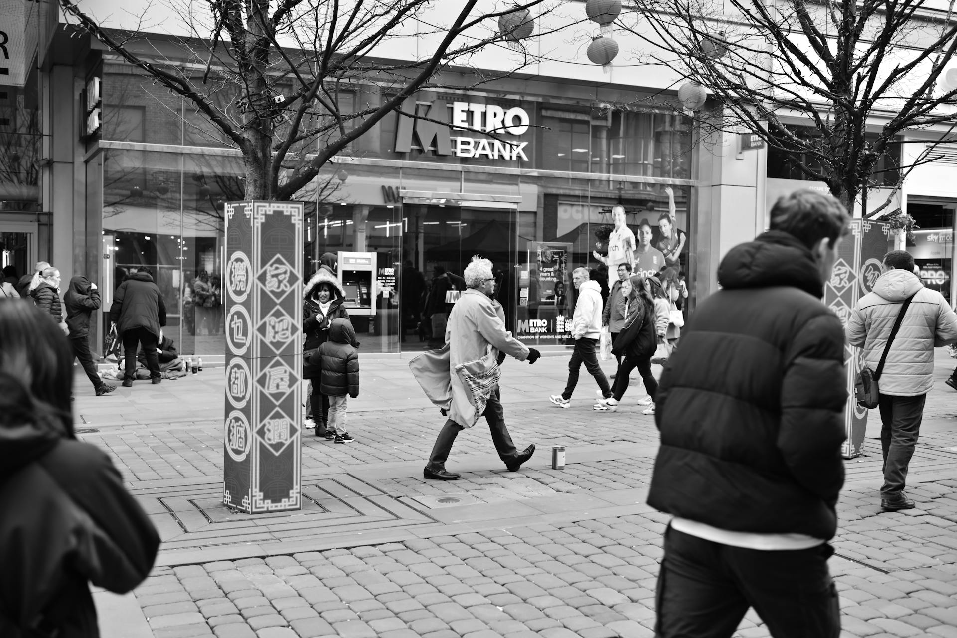 Monochrome street view of people walking past a bank with decorative columns.