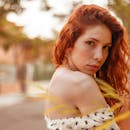 这是一幅在户外自然光线下拍摄的肖像，画中是一位令人惊叹的红发雀斑年轻女子