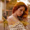 日落时分，一位身着圆点连衣裙、留着红色卷发的女子在户外拍摄时尚肖像