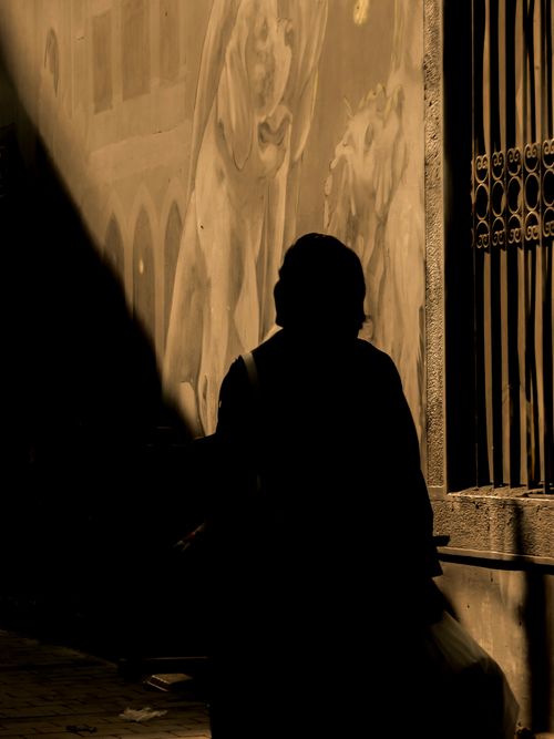 Free Dramatic silhouette of a person walking by a wall with artistic murals, creating a moody atmosphere. Stock Photo