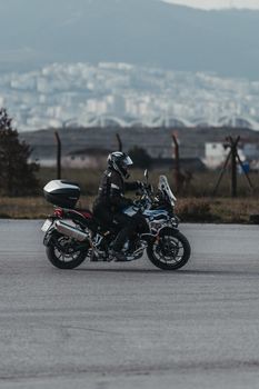 A motorcyclist in full gear rides on a road with a cityscape backdrop.