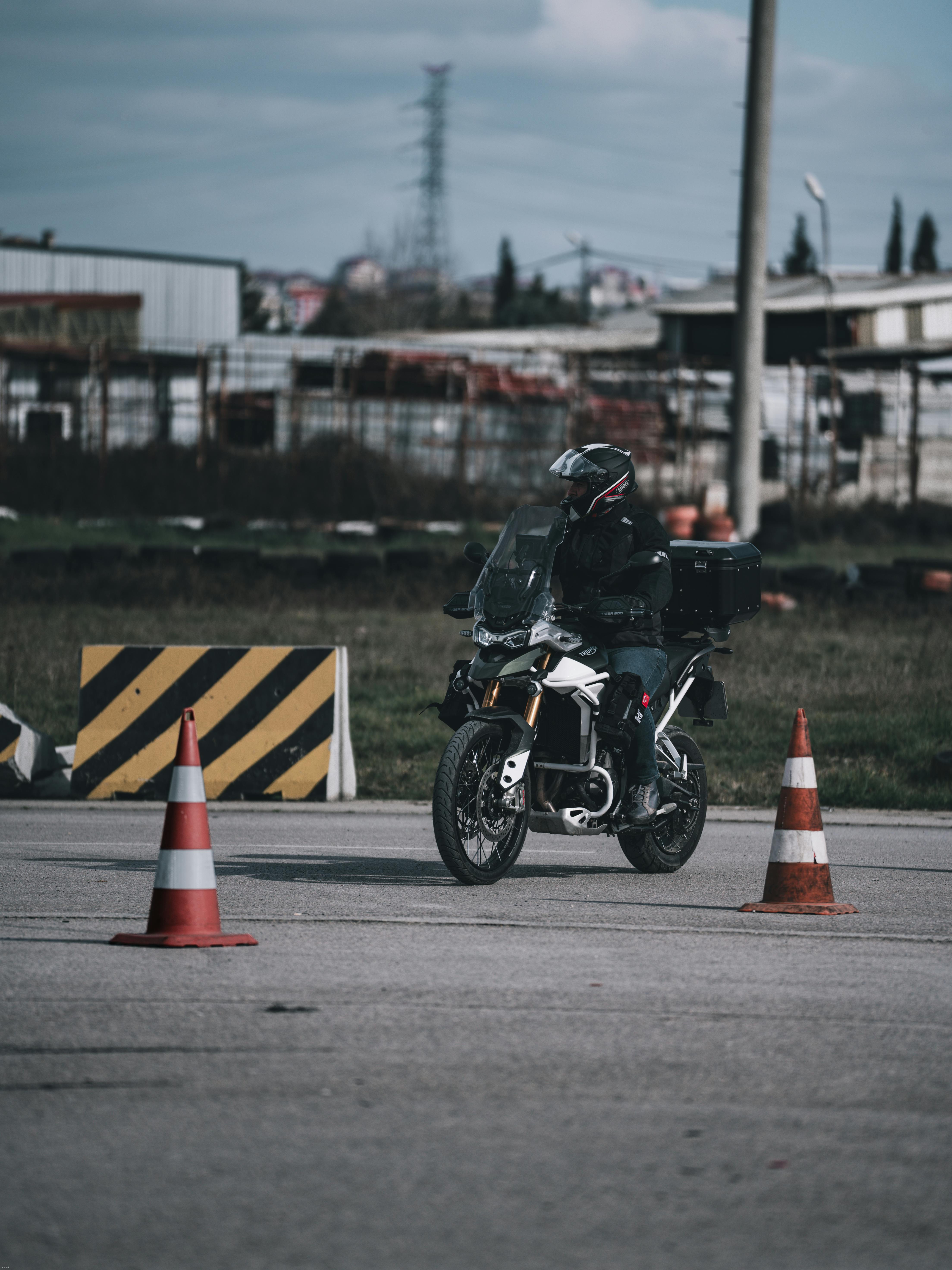 A motorcyclist in gear maneuvers between traffic cones on a sunny day in an industrial area.