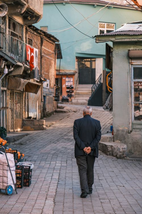 Free Back view of an elderly man walking through a vintage Turkish alley lined with old buildings. Stock Photo
