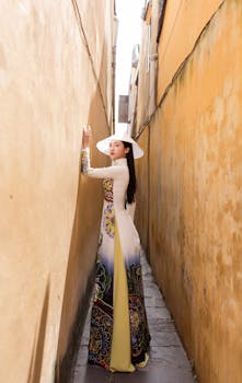 Elegant woman in ao dai standing in a sunlit alley, Hội An.
