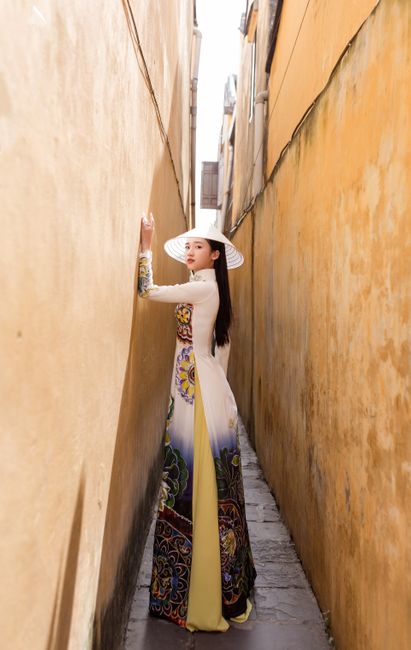 Elegant woman in ao dai standing in a sunlit alley, Hội An.