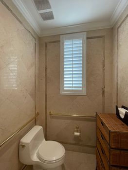 Elegant bathroom interior featuring beige marble tiles, a white toilet, and louvered window. Stylish and compact design.