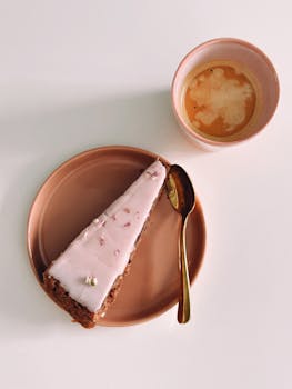 A slice of pink frosted cake with coffee in minimal setting.