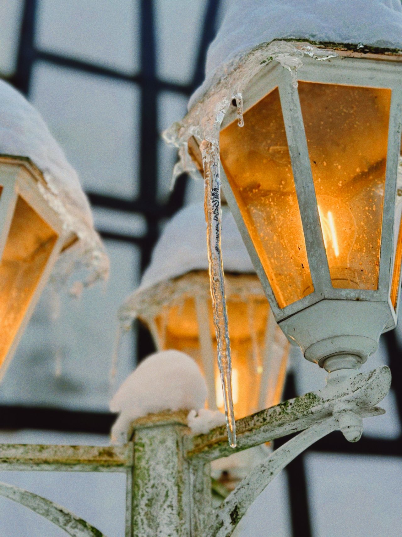 Snow-capped outdoor wall lanterns glowing warmly with icicles hanging from the frame.