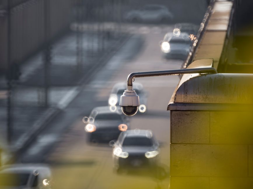 Best Outdoor Security Cameras with Night Vision: Complete 2026 Guide CCTV camera monitoring city traffic on a busy road with blurred vehicles in the background.