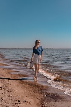 A woman walks along a sandy beach under a clear blue sky, enjoying a sunny day.