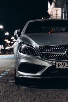 Front view of a luxury silver car parked on an urban street at night.