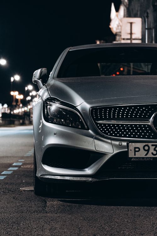 Free Front view of a luxury silver car parked on an urban street at night. Stock Photo