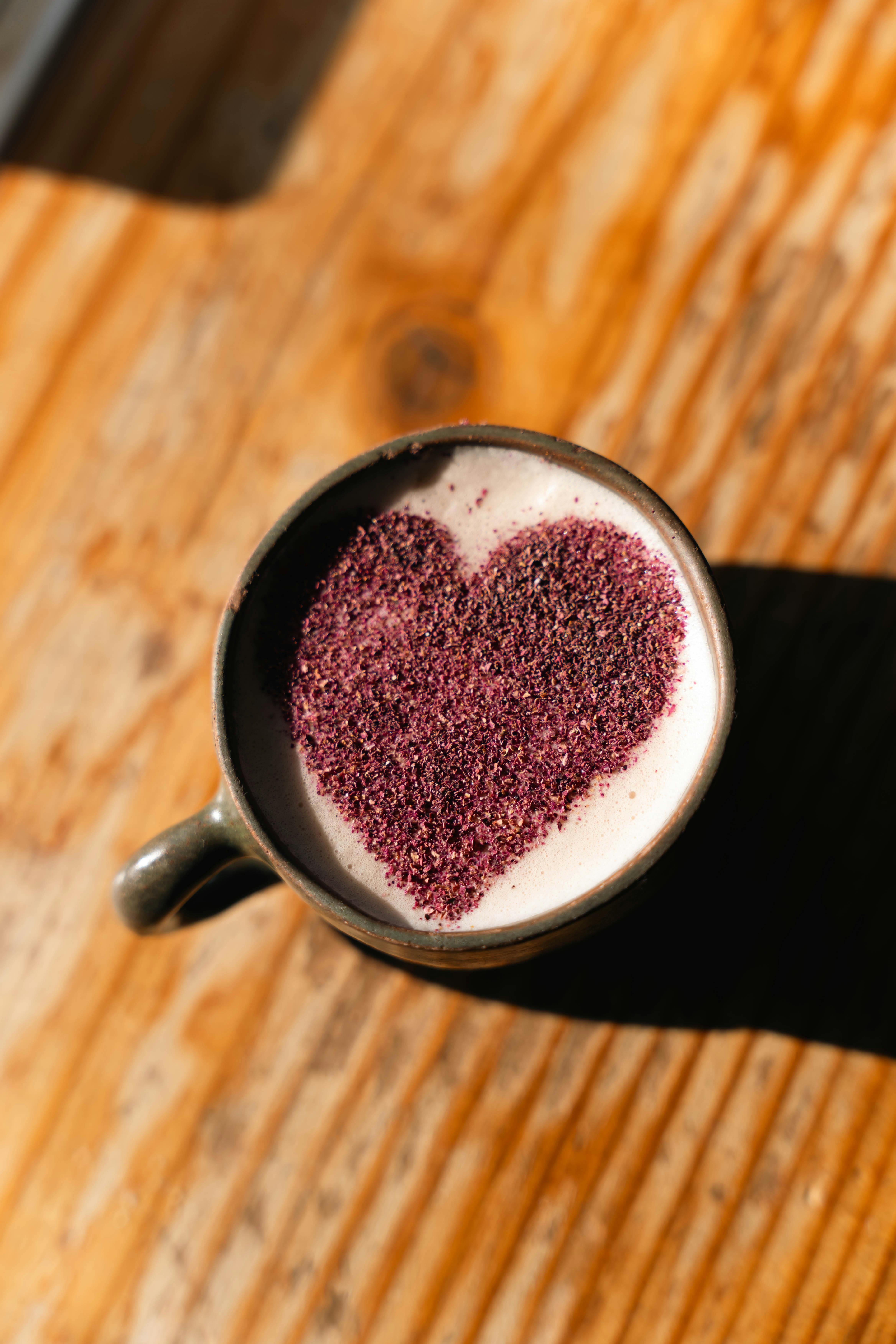 Close-up of latte with heart-shaped cocoa powder design on wooden table.