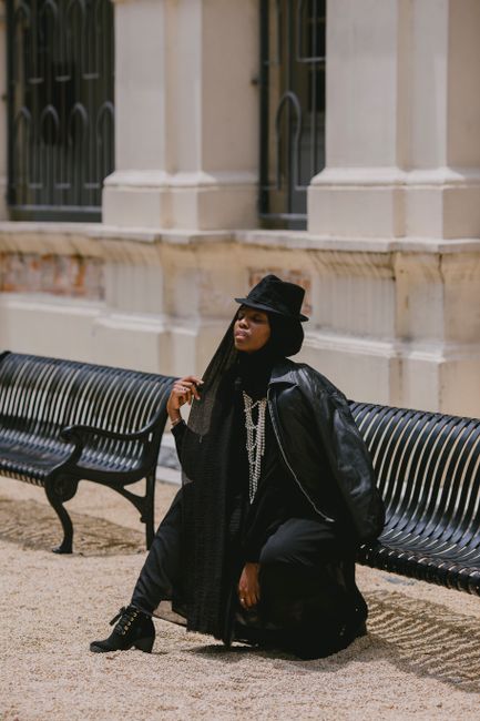 African American woman in a black outfit, sitting stylishly on a bench outdoors.