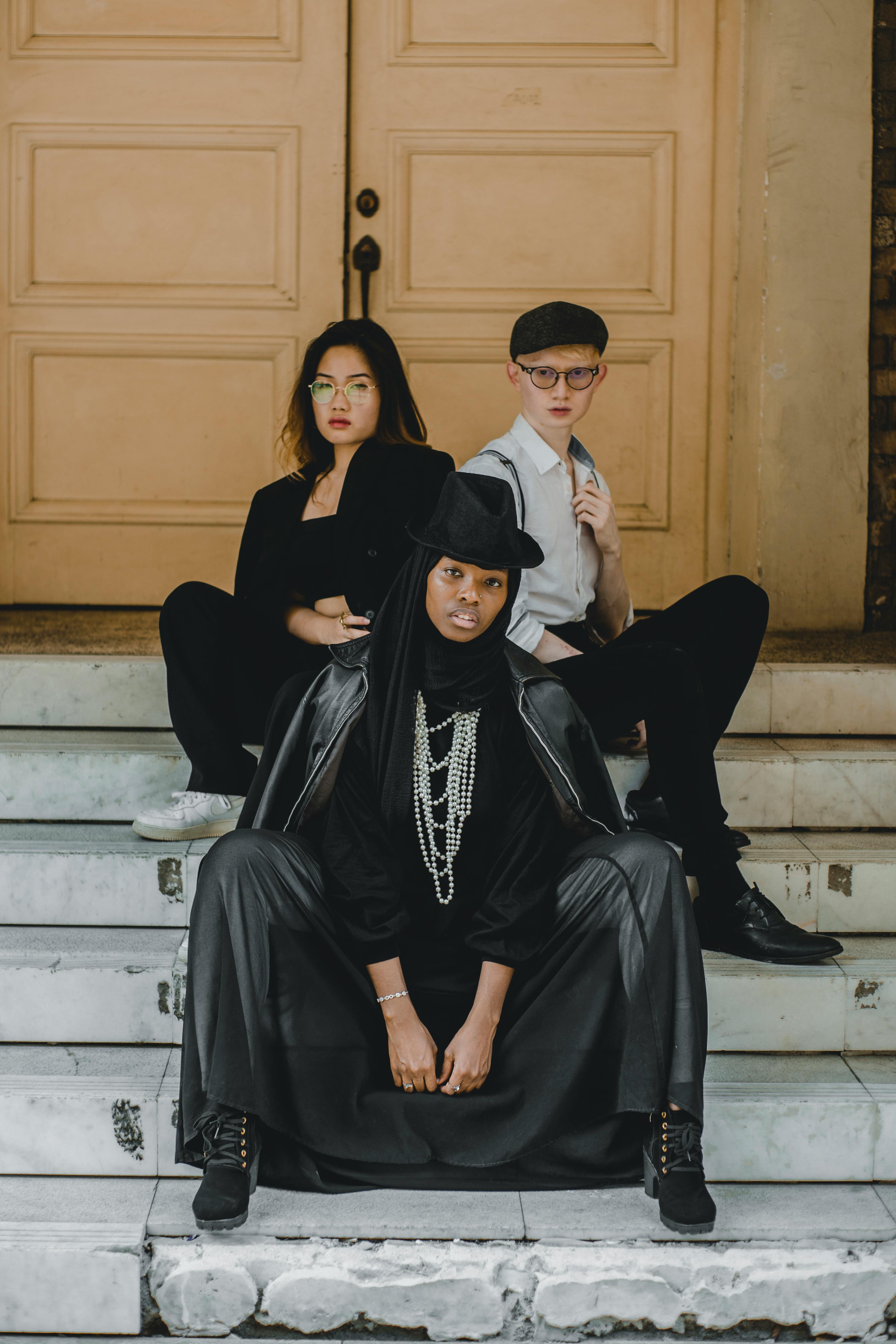 two women and man sitting on gray concrete stairs