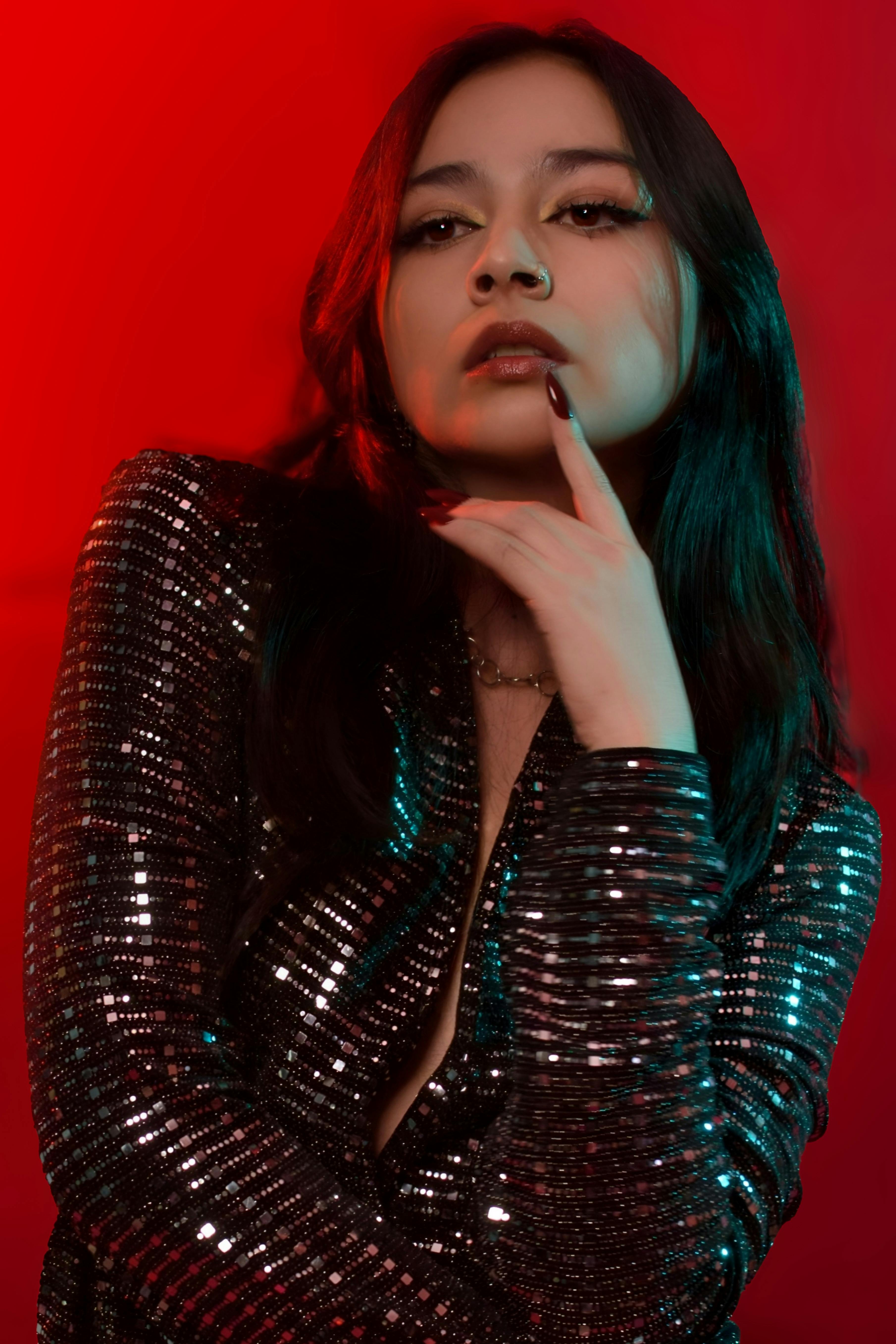 Free A stylish portrait of a young woman posing in a sequin outfit against a bold red background. Stock Photo