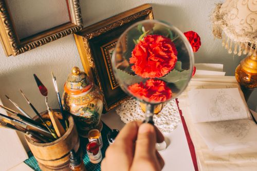 Free A cozy artistic workspace featuring a magnified red carnation, art supplies, and sketchpad. Stock Photo