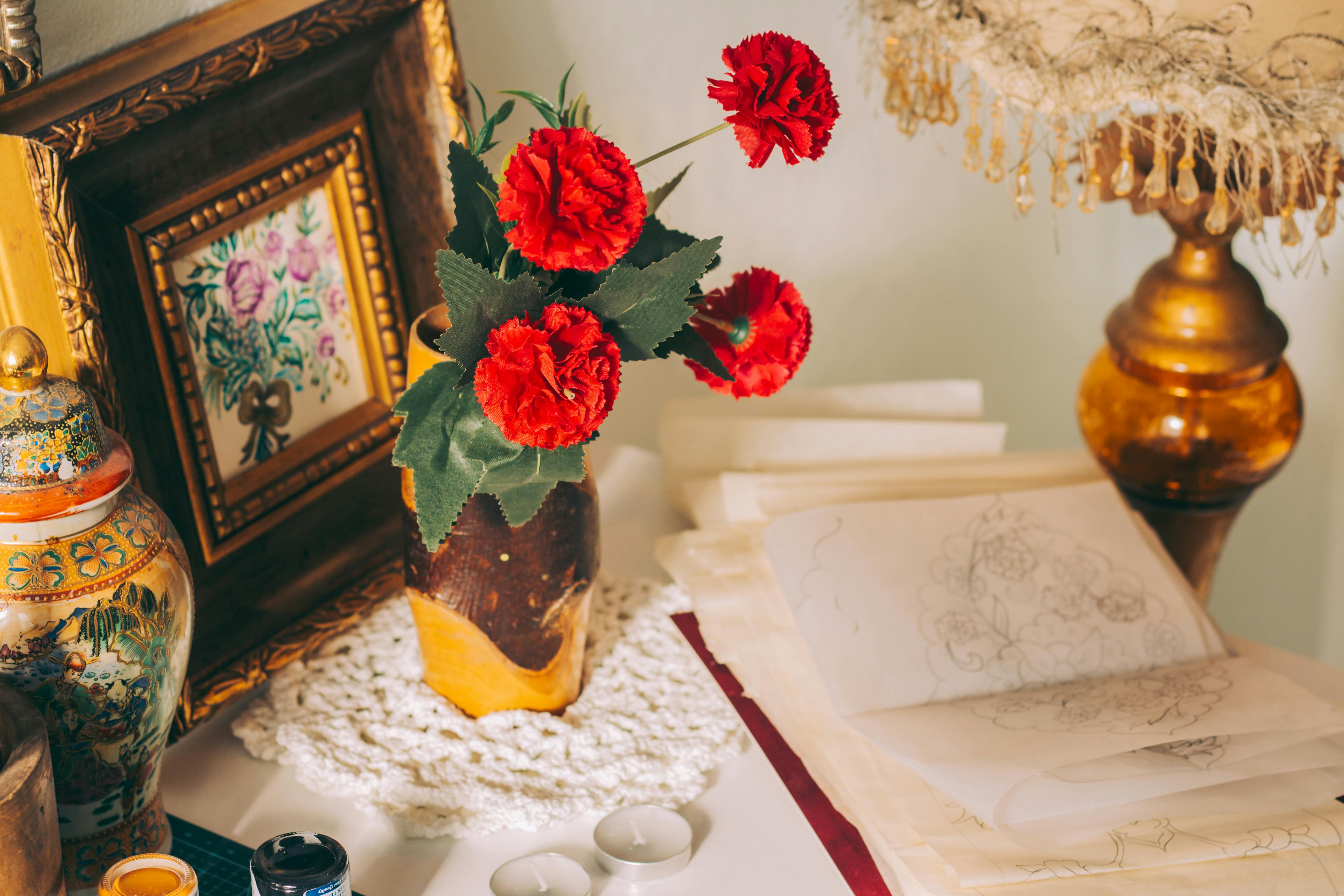 A charming desk arrangement with red carnations, artistic sketches, and vintage decor elements.