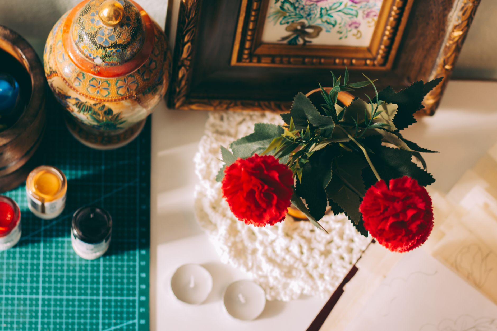 Creative workspace with red carnations, framed art, and ornamental decor.